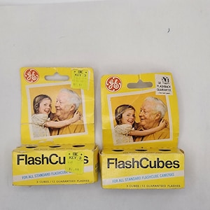 May include: Two yellow boxes of GE Flashcubes for standard flashcube cameras. Each box contains 3 cubes with 12 guaranteed flashes. The boxes have a picture of a young girl and an older man hugging.