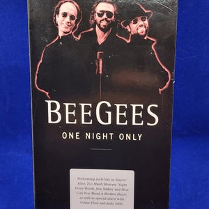Puede incluir: Una caja negra de cinta VHS con los Bee Gees. La portada presenta una foto de los miembros de la banda y el texto "BEE GEES ONE NIGHT ONLY". La parte posterior enumera canciones como "Stayin' Alive".