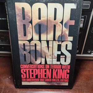 May include: A black book with the title "Bare Bones: Conversations on Terror with Stephen King" in red letters. The book has a red spine and a white background with the authors' names in black letters.