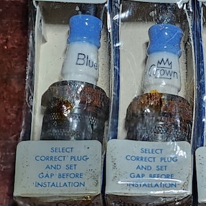 以下が含まれることがあります： 透明なプラスチックパッケージに入ったスパークプラグ2本。スパークプラグには「Blue Crown」と「Crown」のラベルが貼られています。パッケージには、正しいプラグを選択し、取り付け前にギャップを設定する手順が記載されています。