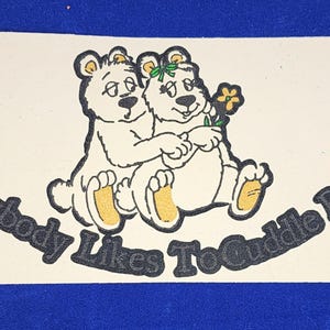 May include: A sticker featuring two cartoon bears embracing, with the text "Everybody Likes To Cuddle Bears" in a curved font. The bears are white with black outlines and yellow accents, holding a flower.