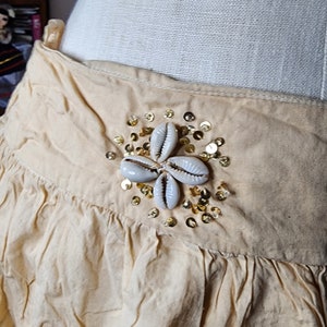 May include: A beige skirt with a decorative embellishment of white seashells and gold sequins.