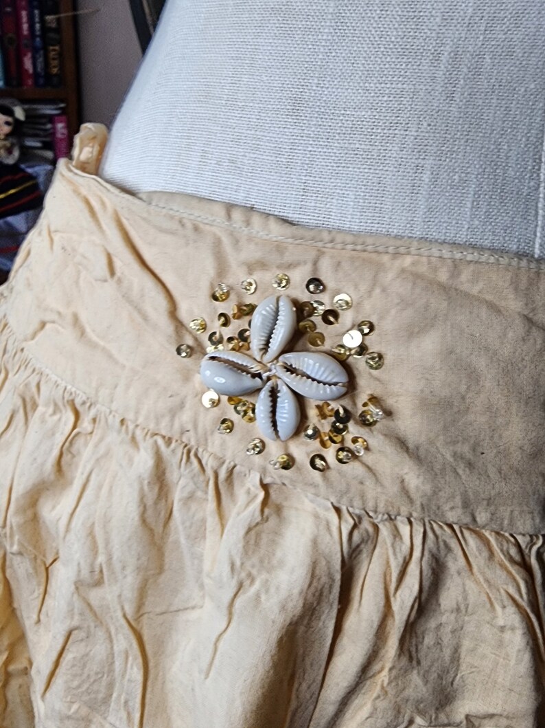 May include: A beige skirt with a decorative embellishment of white seashells and gold sequins.
