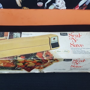 May include: A yellow Sears Seal-N-Save vacuum sealer in its original box. The box features a photo of the sealer and a variety of foods that can be sealed. The text on the box reads "Sears Seal-N-Save" and "Sears Best".