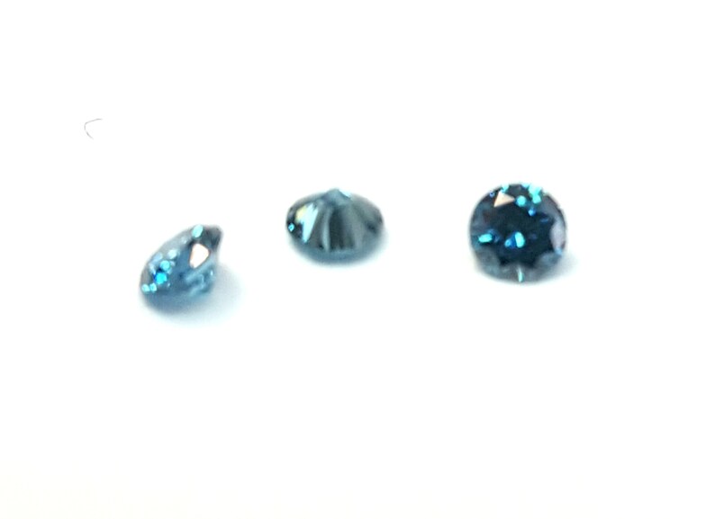 May include: Three small, round, faceted gemstones with a deep blue colour. Each stone features a brilliant cut with multiple reflective surfaces that catch the light, creating a sparkling appearance against a plain white background.