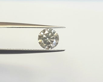 May include: A clear round diamond gemstone held in tweezers. The diamond has a slight yellow tint.