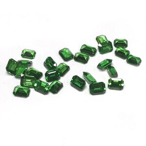 May include: A collection of emerald green gemstones, cut into rectangular shapes, scattered on a white surface.