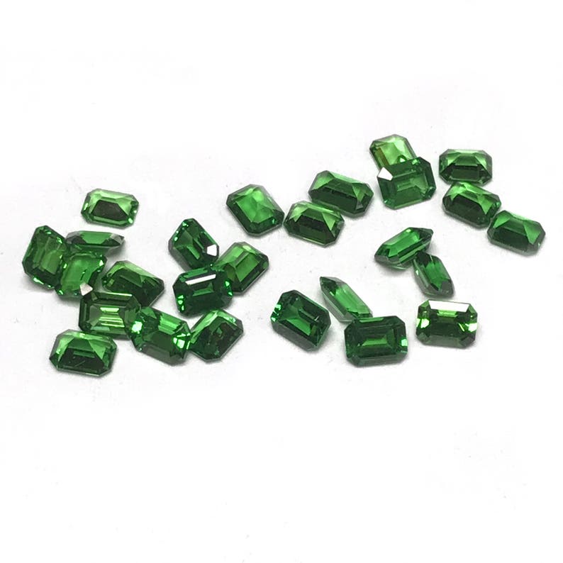 May include: A collection of emerald green gemstones, cut into rectangular shapes, scattered on a white surface.