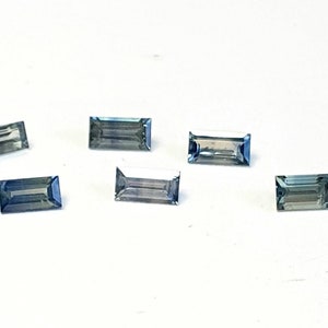May include: Six small, rectangular, blue-green gemstones. The gemstones are faceted and have a slight shimmer.