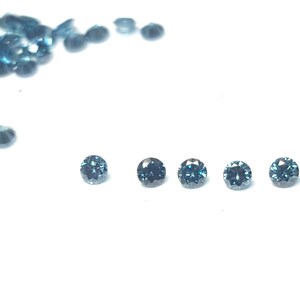 May include: A collection of small, round, faceted gemstones in a deep teal blue colour. Six individual stones are arranged in a horizontal line, while a larger cluster of identical loose stones is scattered in the upper left corner of the frame.