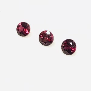 May include: Three round, dark red gemstones with a faceted cut.