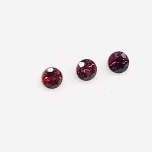 May include: Three round, faceted, dark red gemstones.