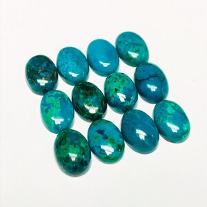 May include: A collection of twelve oval-shaped turquoise cabochons, each with a unique pattern of green and blue hues. The stones are smooth and polished, with a glossy finish.