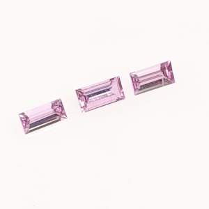 May include: Three pink rectangular gemstones with a faceted cut.