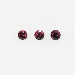 May include: Three round, red gemstones with a dark red center. The gemstones are set against a white background.