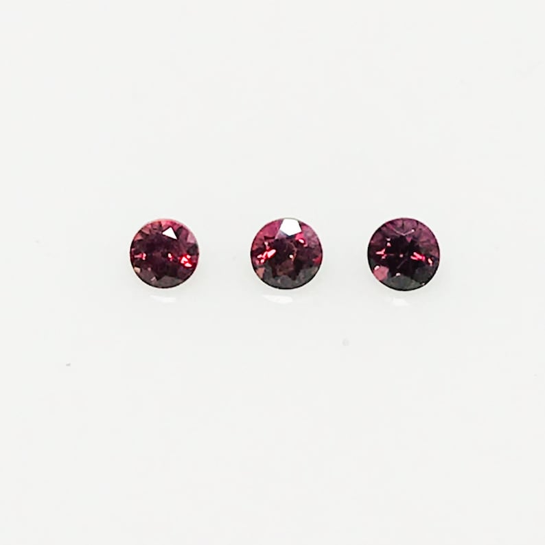 May include: Three round, red gemstones with a dark red center. The gemstones are set against a white background.