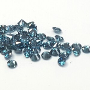 May include: A collection of small, round, faceted gemstones in a deep blue-grey colour. Each stone features a brilliant cut with multiple reflective surfaces that catch the light, creating a sparkling appearance across the cluster of loose gems.