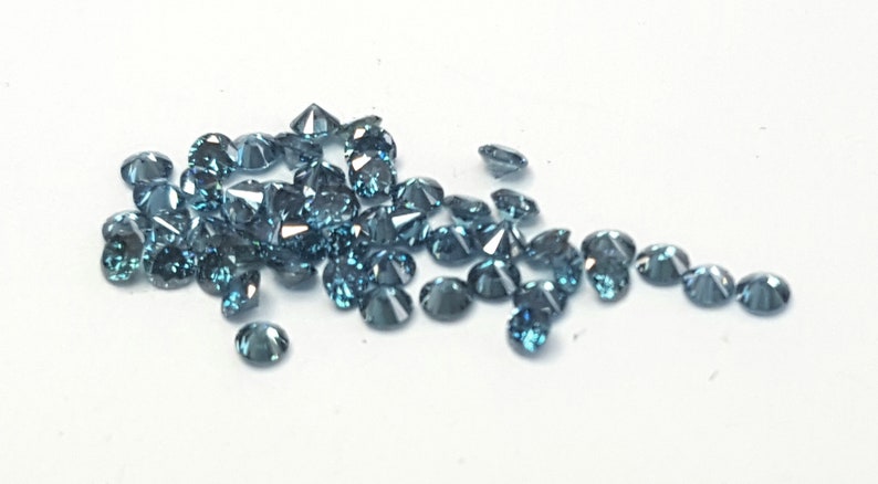 May include: A collection of small, round, faceted gemstones in a deep blue-grey colour. Each stone features a brilliant cut with multiple reflective surfaces that catch the light, creating a sparkling appearance across the cluster of loose gems.