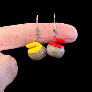 Peut inclure: Une paire de boucles d'oreilles en argent avec des pierres de curling miniatures. Une pierre est peinte en rouge et l'autre en jaune.