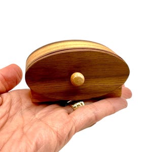 Peut inclure: Une petite boîte en bois avec un tiroir. La boîte est de forme ovale et a une finition en bois brun clair. Le tiroir a un petit bouton en bois.