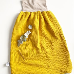 Könnte beinhalten: Ein gelber Schlafsack aus Baumwollmusselin mit einem beigefarbenen gerippten Strickkragen. Der Schlafsack hat eine geraffte Taille und ist aus einem weichen, atmungsaktiven Stoff gefertigt.