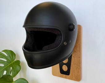 May include: A matte black full-face motorcycle helmet mounted on a wall-hanging display. The display consists of a rectangular light-toned wooden board with a black metal bracket featuring two circular cutouts that supports the helmet.