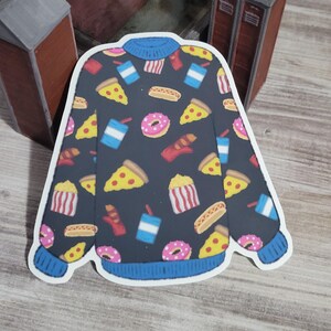 May include: A black sweater with a white outline, featuring a pattern of various foods including pizza, donuts, hot dogs, popcorn, and soda.