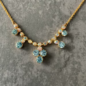 May include: A gold necklace with a delicate chain and a cluster of light blue iridescent rhinestones hanging from the centre.