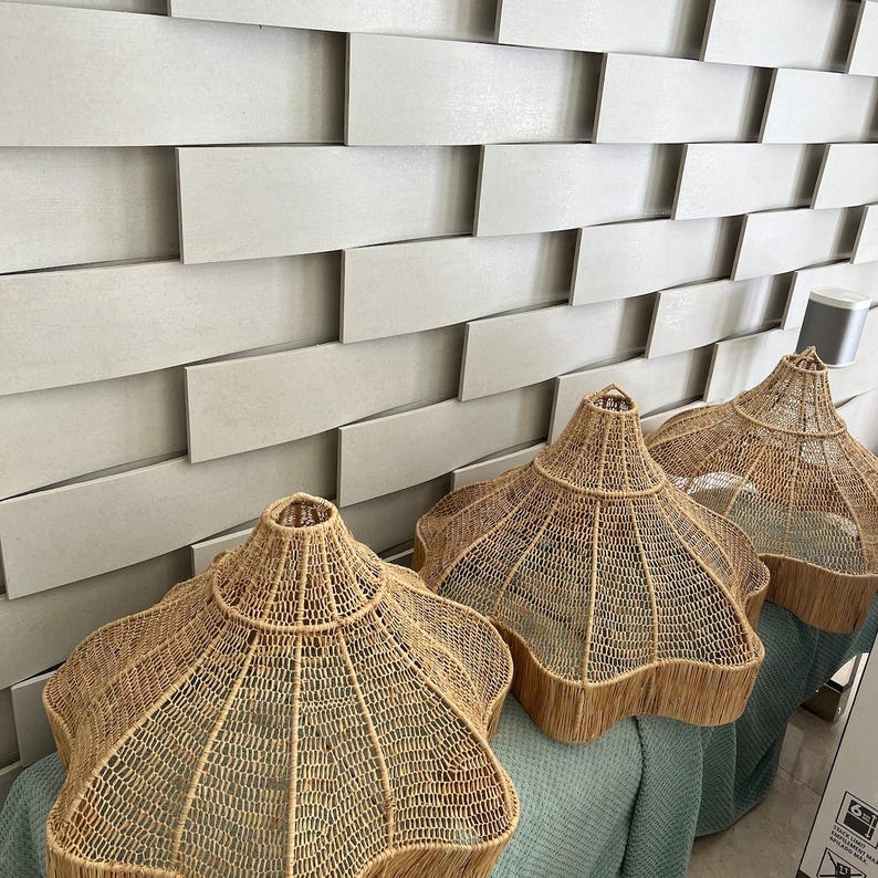 Op de afbeelding: Drie geweven rotan lampenkappen met een uniek stervormig ontwerp. De lampenkappen hebben een natuurlijke bruine kleur en een gefranjerde rand. Ze worden getoond tegen een getextureerde, lichtgrijze muur.