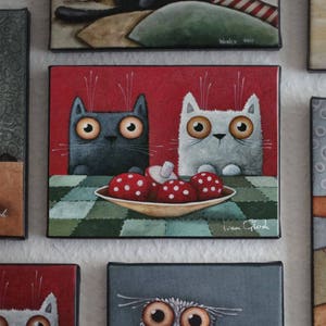 Puede incluir: Una pintura de dos gatos, uno negro y otro blanco, sentados a una mesa con un plato de champi&ntilde;ones rojos y blancos. El fondo es un patr&oacute;n de cuadros rojos. La pintura est&aacute; firmada "Ivan Glod".