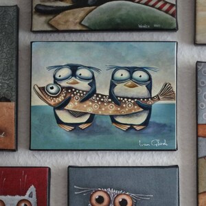 May include: Two cartoon penguins with large eyes and beaks are carrying a brown and white fish with black spots. The fish is longer than the penguins. The background is a light blue. The painting is signed "Ivan Glod".