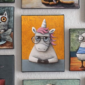 May include: A white unicorn with a pink mane and a blue and black pair of glasses is sitting at a desk. The background is a yellow canvas with a pattern of black lines and circles. The unicorn is looking at the viewer.