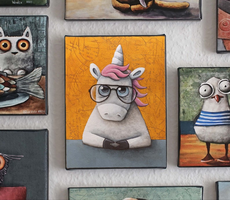 May include: A white unicorn with a pink mane and a blue and black pair of glasses is sitting at a desk. The background is a yellow canvas with a pattern of black lines and circles. The unicorn is looking at the viewer.