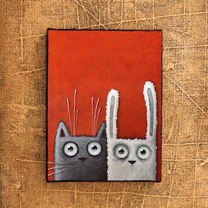 May include: A gray cat and a white rabbit with large eyes are looking to the right. They are on a red background.