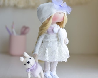 May include: A white doll with blonde hair wearing a white dress, white hat with a purple flower, and white shoes. The doll is holding a small white stuffed animal with purple ears and a purple bow.