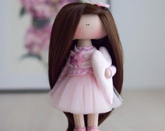 May include: A handmade doll with long brown hair, wearing a pink dress with white polka dots and a white heart-shaped accessory. The doll is wearing pink sneakers with white accents.