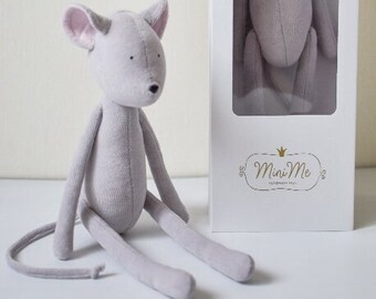 May include: A gray plush mouse toy with long limbs and a long tail. The mouse is sitting on a white surface. The mouse is packaged in a white box with the text "Mini Me" printed on the front.
