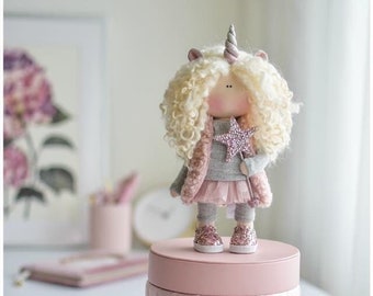 May include: A pink quilted box with a unicorn doll on top. The doll has a grey sweater, pink skirt, and sparkly shoes. The doll is holding a sparkly star wand.