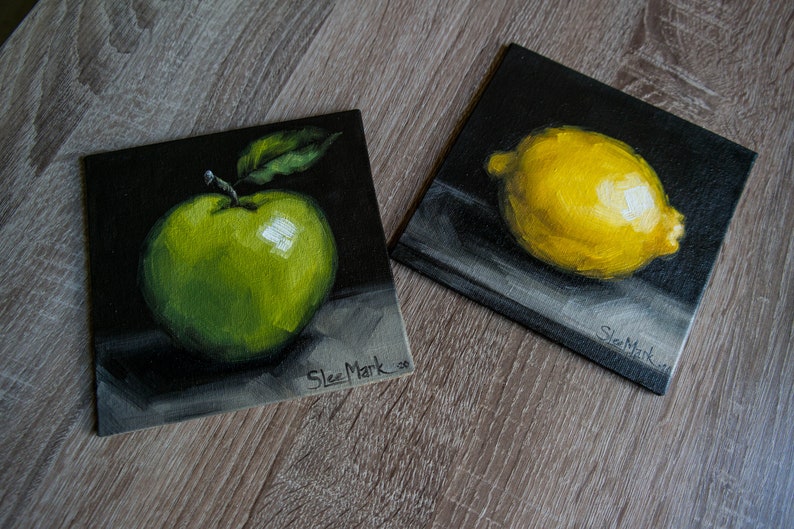 May include: Two small paintings on black canvases, one with a green apple and the other with a yellow lemon. Both paintings are signed "Slee Mark".
