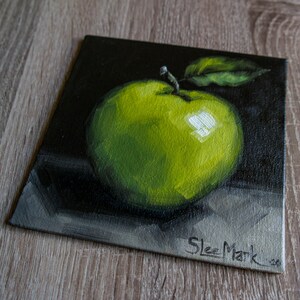 May include: A small painting of a green apple with a leaf on a black background. The artist's signature, "Skee Mark", is in the bottom right corner.