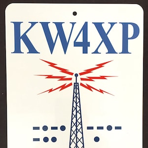 May include: A white sign with blue text and a red and blue illustration of a radio tower. The sign reads "KW4XP Covington, Kentucky U.S.A."