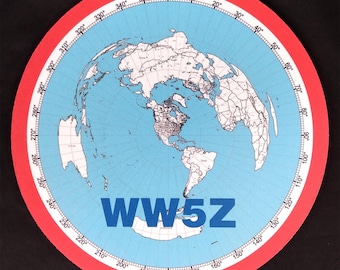 May include: A red and blue world map with a white outline of the continents. The map is on a round, red background with a white circle around the edge. The circle has numbers from 0 to 360 degrees marked on it. The text "WW5Z" is in blue letters in the center of the map.