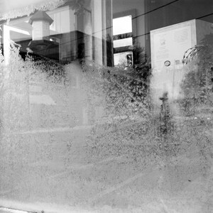 May include: A black and white photo of a window with frost on the glass. The frost creates a blurry, abstract pattern on the glass. The window looks out onto a building with a sign that says "The Book Nook".