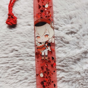 May include: A red resin bookmark with a cartoon character and a red tassel. The bookmark is filled with red glitter and a cartoon image. The tassel is made of red yarn.