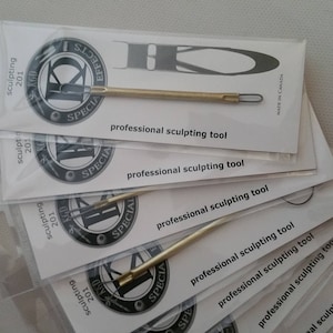 May include: Several professional sculpting tools, each in a clear plastic sleeve. The tools have a brass-coloured handle and a loop at the end. The packaging includes the text "sculpting 201" and "professional sculpting tool".