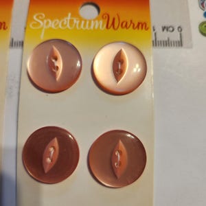 May include: Four round, peach-colored buttons arranged in a two-by-two grid on a Spectrum Warm display card. Each button features a central, elongated diamond-shaped indentation with two holes for thread, showing a smooth, glossy finish.