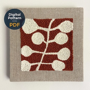 May include: A square punch needle embroidery piece featuring a central stem with rounded off-white leaves against a deep rust-colored background, framed by a natural tan burlap border. A circular blue badge with the text Digital Pattern PDF is visible.