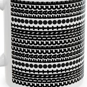 May include: A white ceramic mug featuring a repeating black graphic pattern of horizontal bands. The design consists of rows of stylized letters, circles, plus signs, and zig-zag lines arranged in a stacked, geometric, and monochromatic layout.