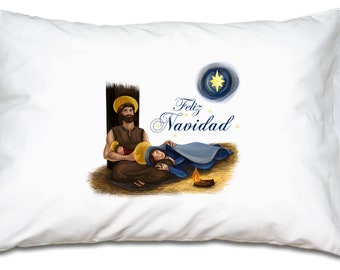 Puede incluir: Una almohada blanca con una representación de la escena de la natividad. La imagen muestra a José, María y el niño Jesús. El texto "Feliz Navidad" está escrito en cursiva azul sobre la escena. Una estrella está en la esquina superior derecha de la imagen.