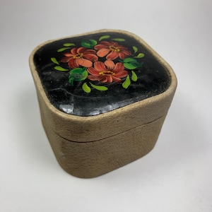May include: A small square box with a beige exterior and a black lid. The lid is decorated with hand-painted red and green flowers.